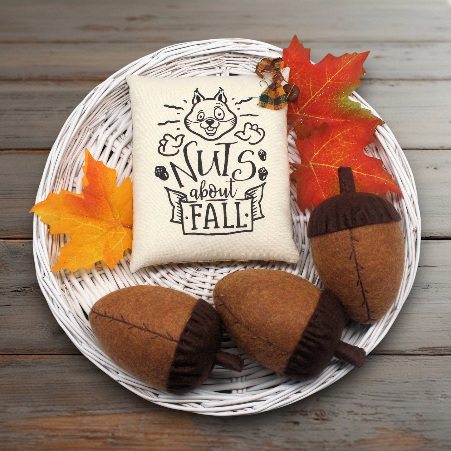 Decorative pillow with 'Nuts about Fall' text on a plate with acorns and leaves.