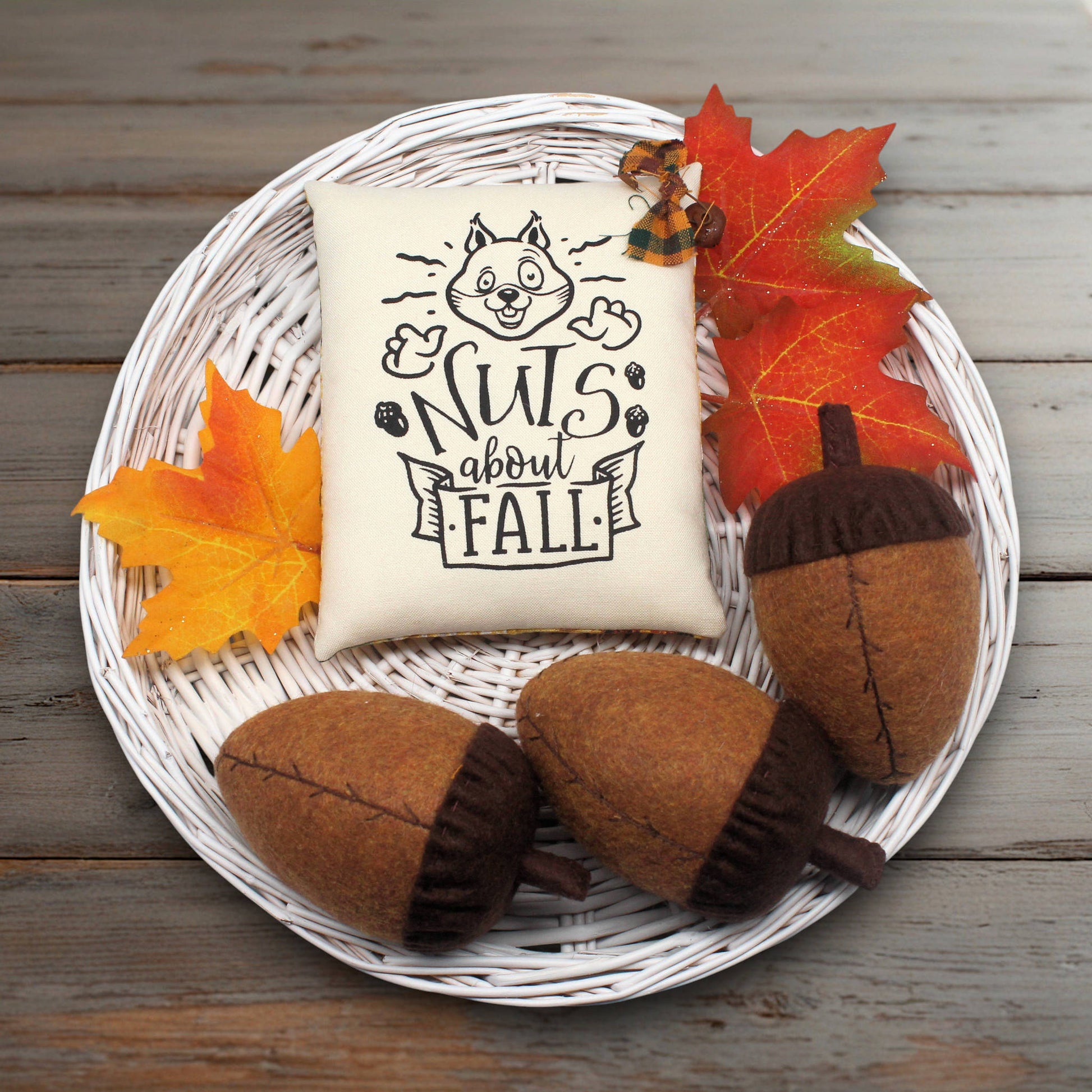 Decorative pillow with 'Nuts about Fall' text on a plate with acorns and leaves.