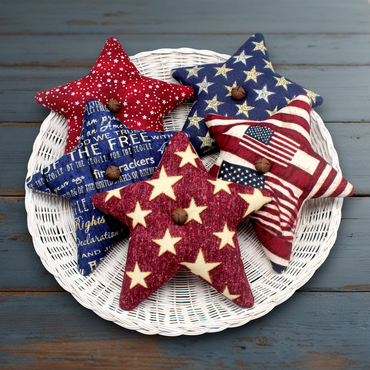 Set of five country primitive fabric stars sewn from coordinating Americana print fabrics with rusty bells stitched to the centers