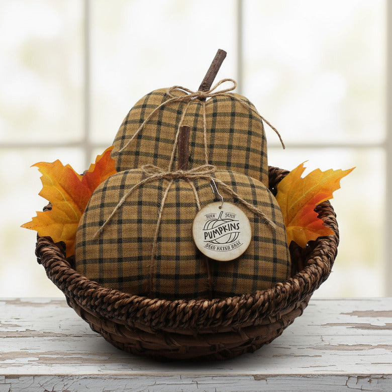 Decorative homespun fabric pumpkins with plaid pattern in a woven basket with fall leaves on a light background