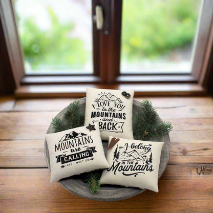 Three mini pillows with mountain-themed text in a decorative bowl on a wooden surface.