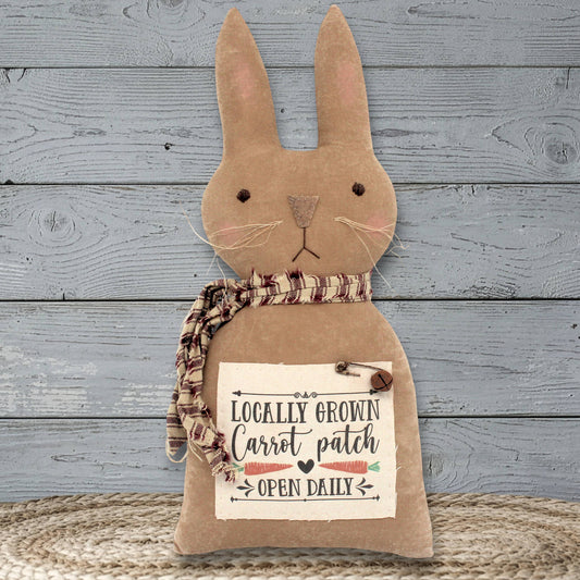 Decorative primitive style bunny rabbit with a scarf and 'Locally Grown Carrot Patch' text on a wooden background