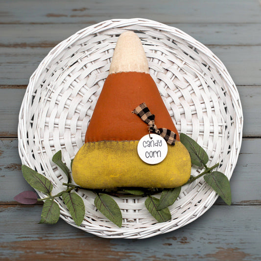 Decorative candy corn with a label on a white woven plate with leaves against a wooden background