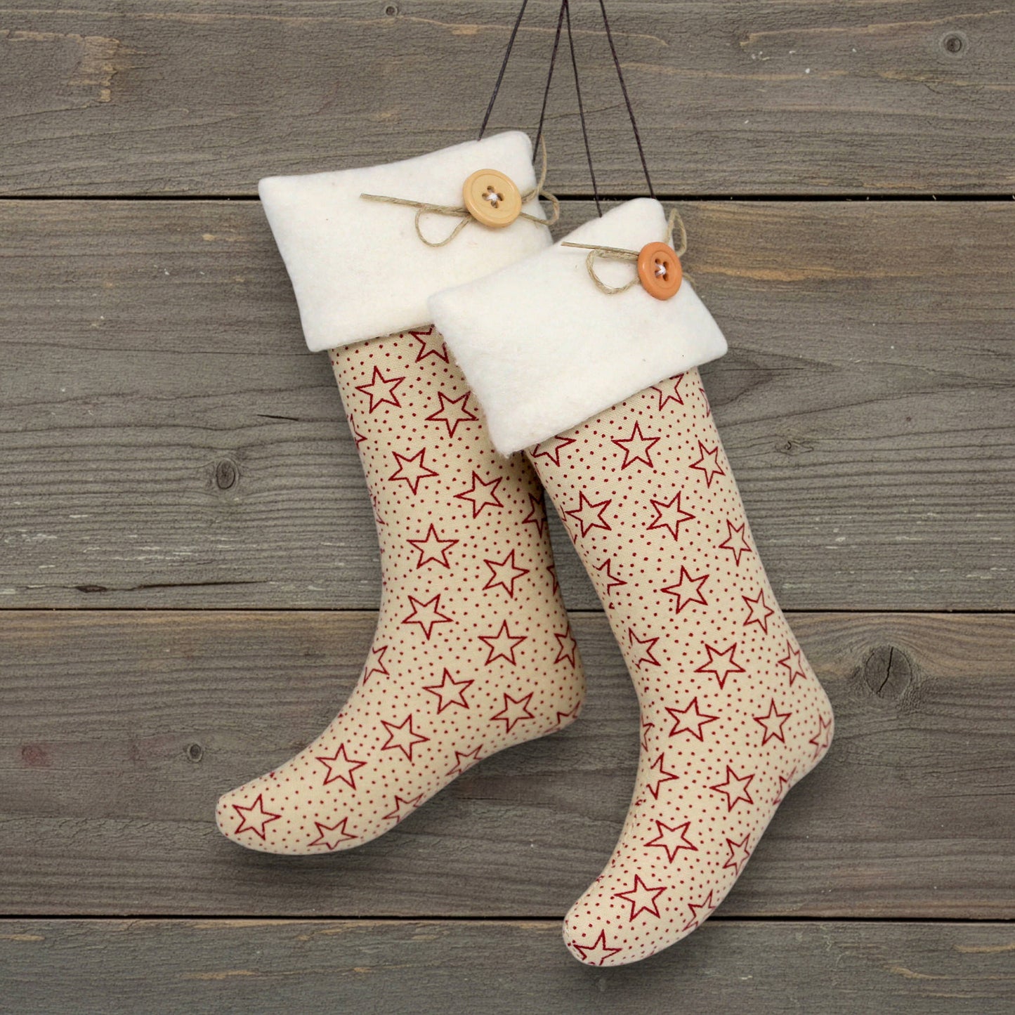Pair of handmade country primitive Christmas stocking ornaments with red stars on a tan background