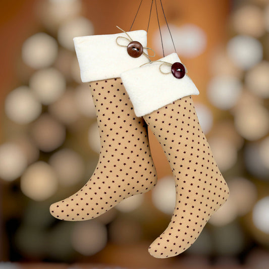 Two tan Christmas stockings with small burgundy stars and white fleece cuffs, hanging against a warm, blurred holiday background.