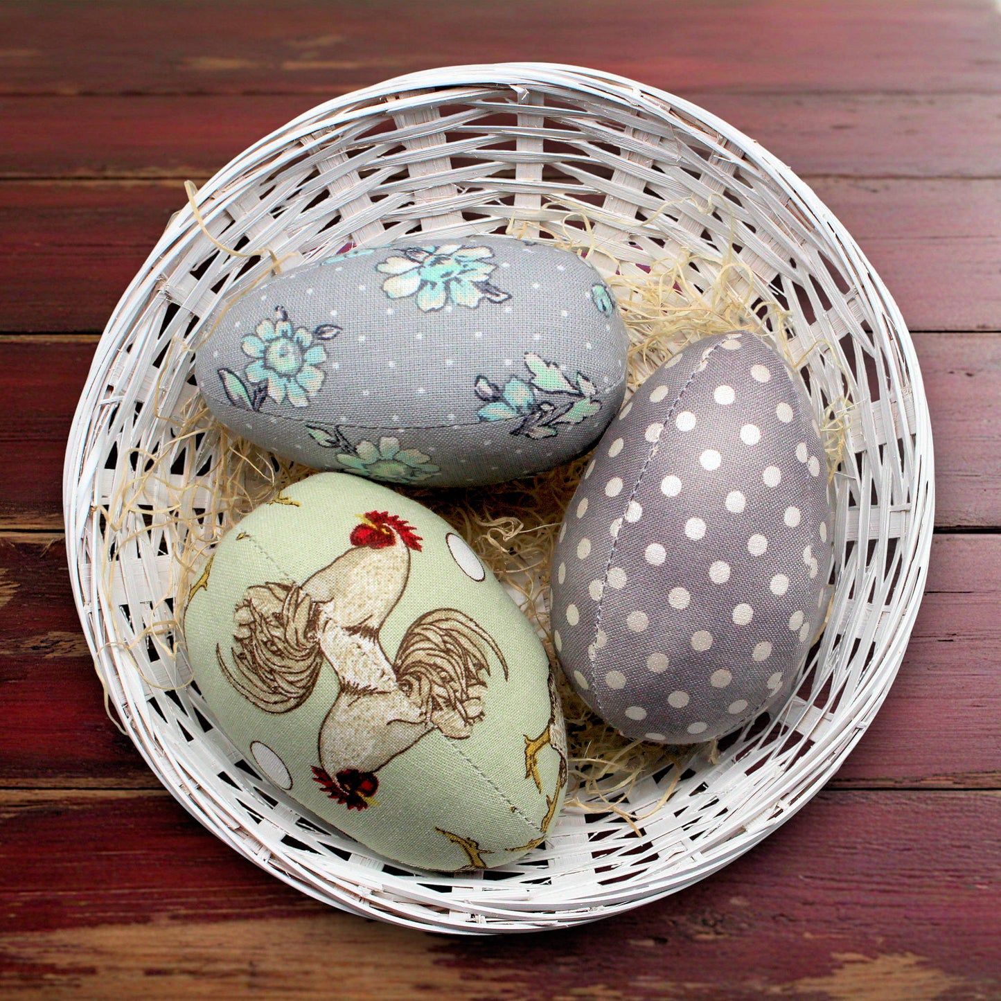 Decorative eggs with floral, rooster, and polka dot patterns in a white basket on a wooden surface.