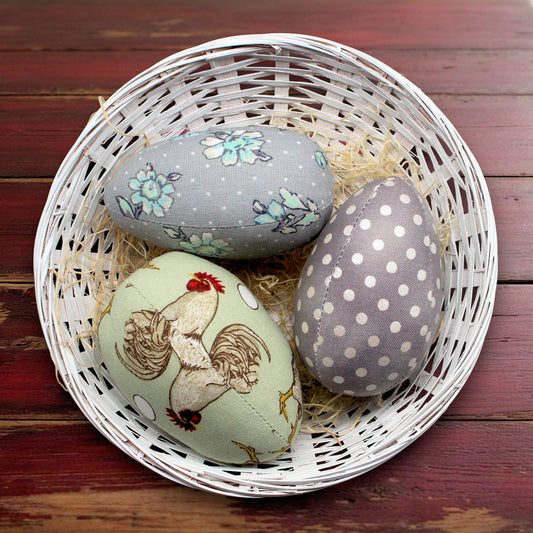 Decorative eggs with floral, rooster, and polka dot patterns in a white basket on a wooden surface.