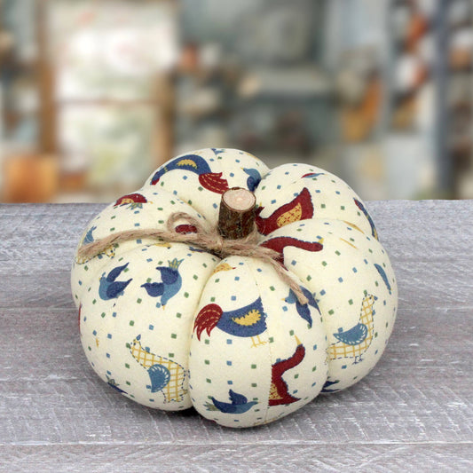 A fabric decorative pumpkin with a cream-colored background, printed with folk art birds and small green dots, tied with a rustic twine bow and topped with a small wooden stem.