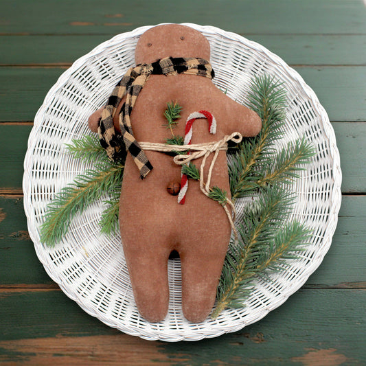 Primitive gingerbread doll with Christmas elements on a white woven plate against a wooden background