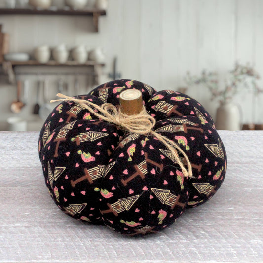 A fabric pumpkin decoration with a black background, printed with pink hearts, brown trellis patterns, and small green strawberry motifs, tied with natural jute twine and topped with a wooden stem.
