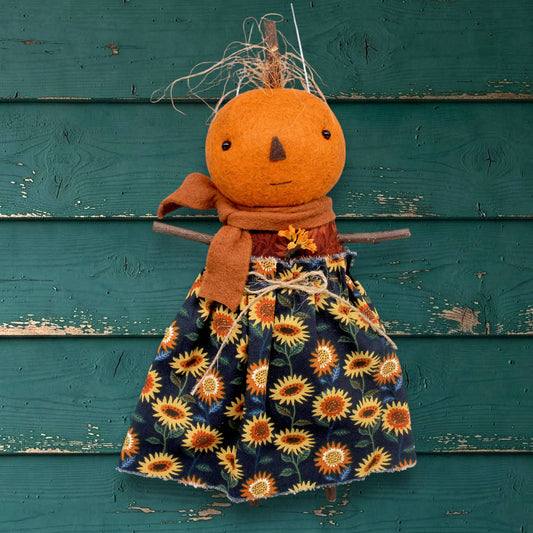 Pumpkin character doll with a sunflower dress against a teal wooden background