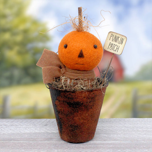 Small primitive doll in a faux rusty bucket with a pumpkin head made from wool felt.  There's a sign that reads 'punkin patch.' The little doll wears a scarf and has wispy coconut fibers surrounding his stem.