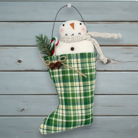 Green plaid Christmas stocking with a snowman decoration on a wooden background