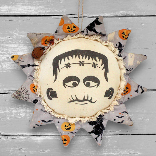 Primitive handmade sunflower ornament with a printed center featuring an image of a spooky Halloween monster face.
