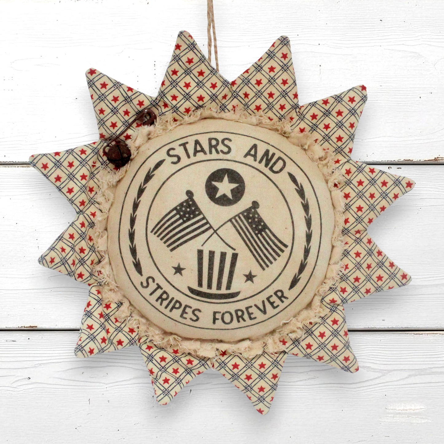 A rustic sunflower ornament hanging wall decor piece with a central round label reading “STARS AND STRIPES FOREVER” and crossed American flags, surrounded by patterned fabric rays in red, white, and blue on a white wood plank background.