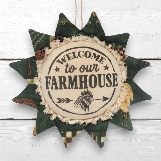 A rustic fabric sunflower ornament hanging sign with a central cream circle reading “WELCOME to our FARMHOUSE” and a black lion illustration, surrounded by dark green patterned fabric rays.