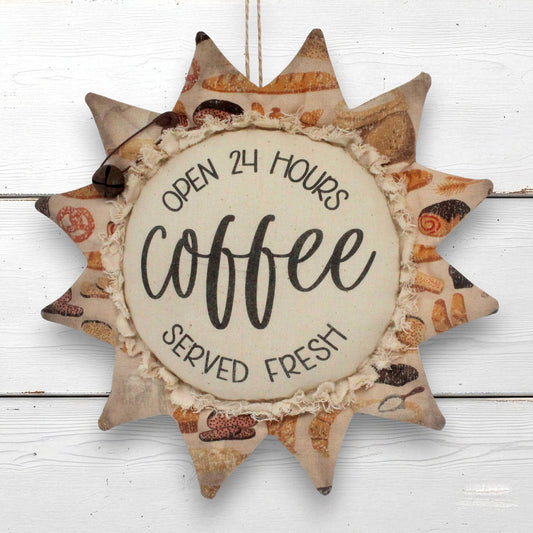 A decorative sunflower ornament wall hanging with a rustic fabric design, featuring the words 'OPEN 24 HOURS coffee SERVED FRESH' on a light beige center panel, shown hanging against a white wood plank background.