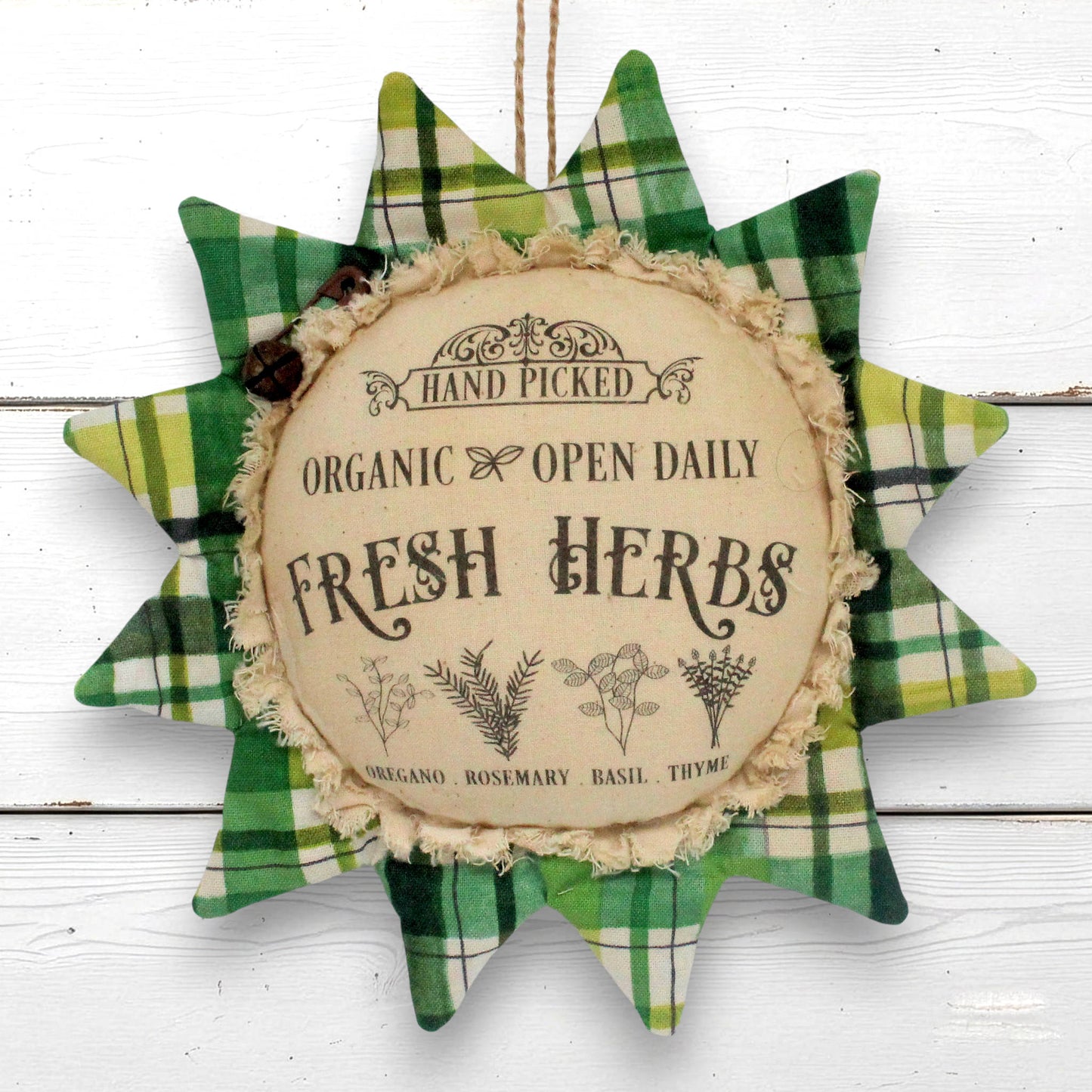 A decorative primitive sunflower fabric ornament with a green and yellow plaid outer border and a central beige circle reading 'Fresh Herbs' and 'Hand Picked Organic Open Daily,' shown against a white wood background.