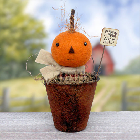 Small primitive doll in a faux rusty bucket with a pumpkin head made from wool felt.  There's a sign that reads 'punkin patch.' The little doll wears a scarf and has wispy coconut fibers surrounding his stem.