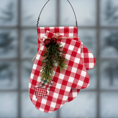 A Christmas ornament with overlapping homespun fabric mittens in red and white decorated with faux pine and jingle bells