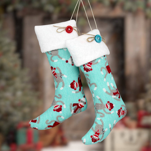 Two hanging Christmas stockings with white fleece cuffs, one with a red button and one with a blue button, printed with red and gray sock monkeys on a turquoise background.