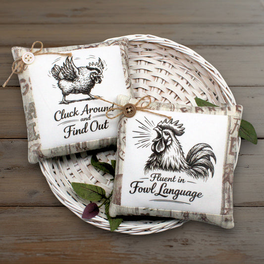 Set of two mini pillow bowl fillers featuring wise-cracking chickens or roosters with humorous messaging displayed in a white basket on a wooden table