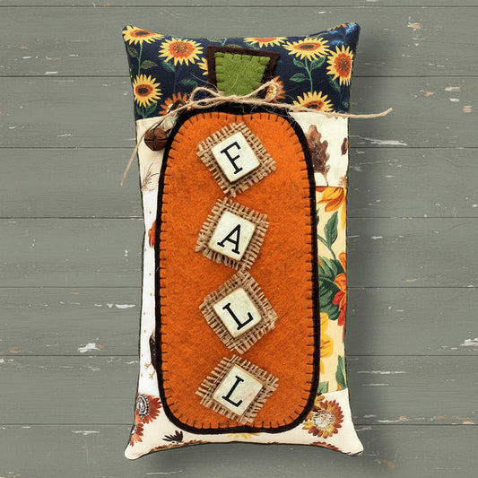 Decorative pillow with 'FALL' letters and autumn-themed design on a white wooden background