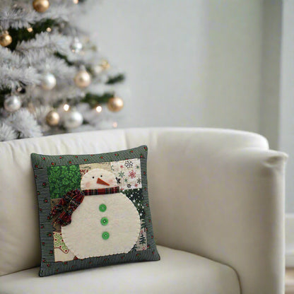 Decorative pillow with a snowman design on a white couch with a Christmas tree in the background.