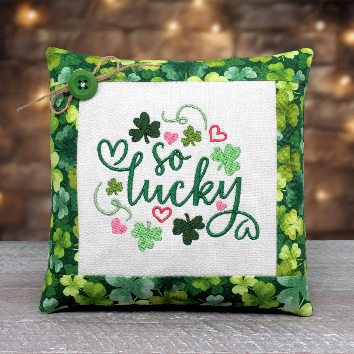 Small pillow tuck or bowl filler embroidered with 'so luck' along with pink hearts and shamrocks.  The center panel is trimmed with a print fabric with a colorful green shamrock design.