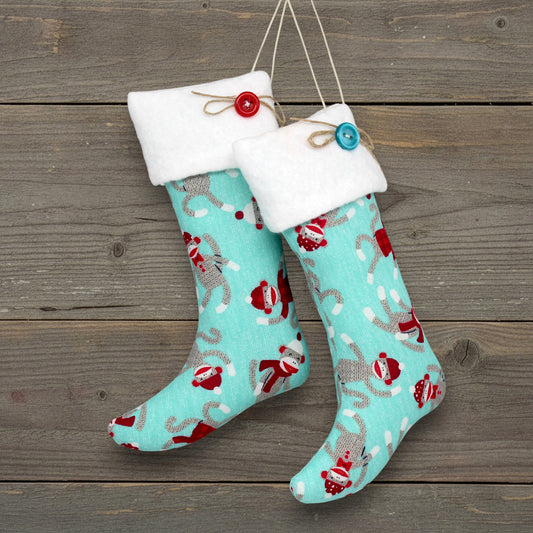 Pair of handmade Christmas stocking ornaments with a sock monkey pattern on a greenish blue background