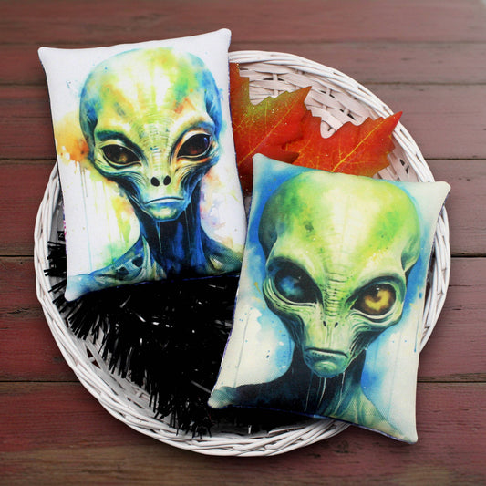 Two alien-themed pillows on a woven basket with autumn leaves.