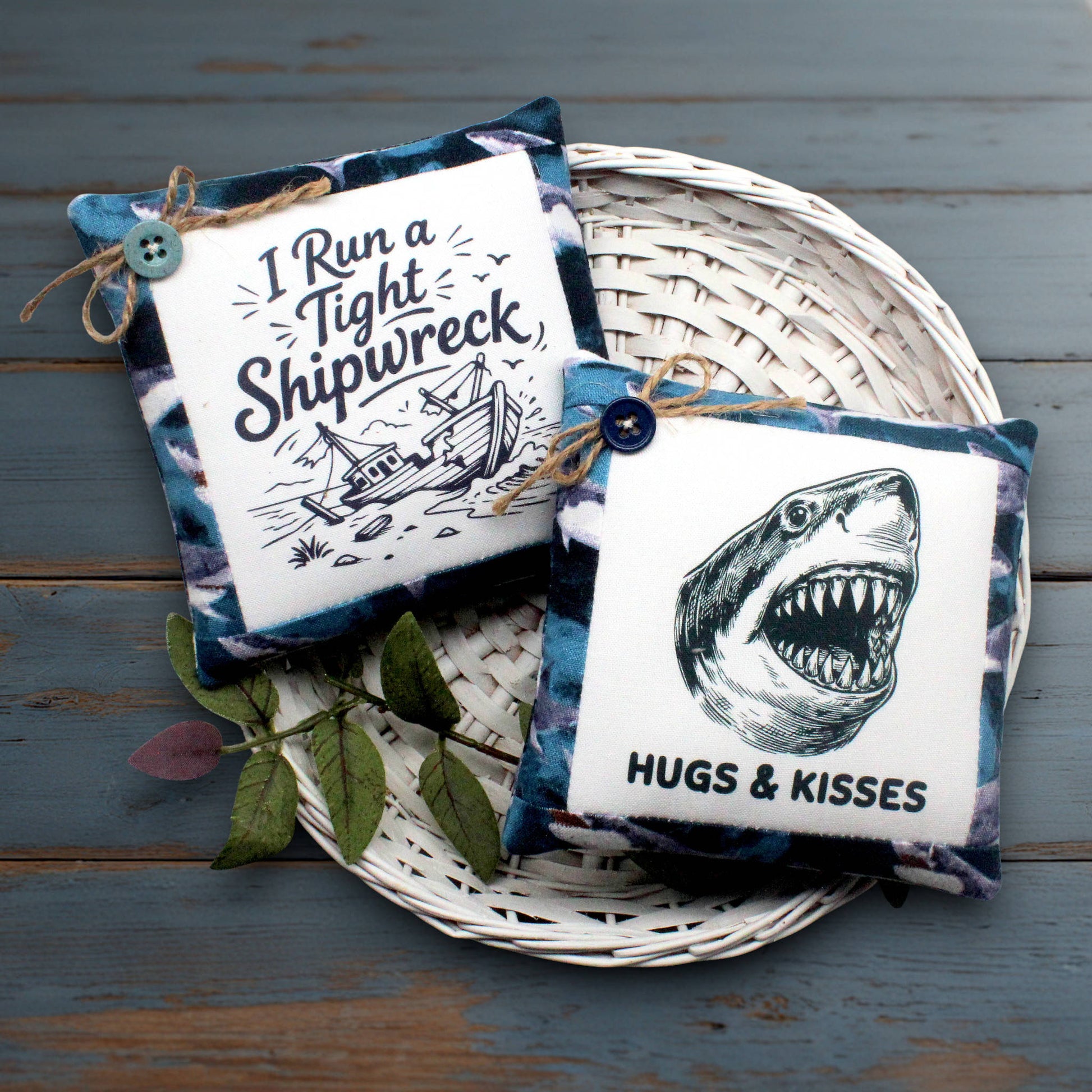 Two square fabric mini pillows displayed on a white woven tray over a rustic blue wooden surface. One pillow has a white center with black text reading 'I Run a Tight Shipwreck' and a ship illustration, bordered in blue patterned fabric.