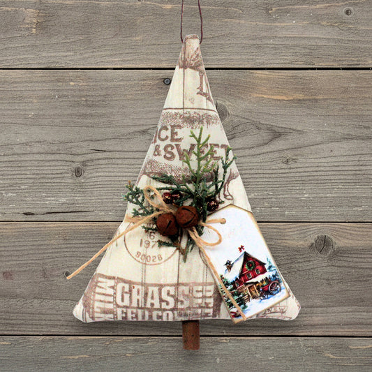 A rustic Christmas tree-shaped fabric hanging ornament made from vintage-style printed fabric with a farmers market design, decorated with green pine branches, rusty bells and a small printed tag, shown against a weathered wood plank background.
