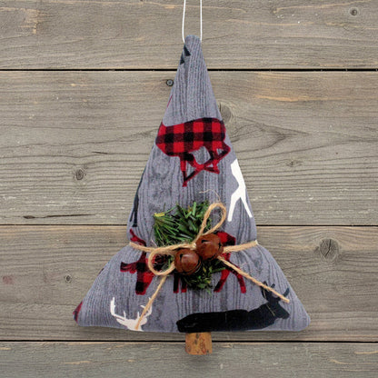 A fabric Christmas tree ornament made from gray corduroy with red and black buffalo plaid forest animals, green pine branches, and two rusty bells tied with twine, hanging against a rustic wood plank background.