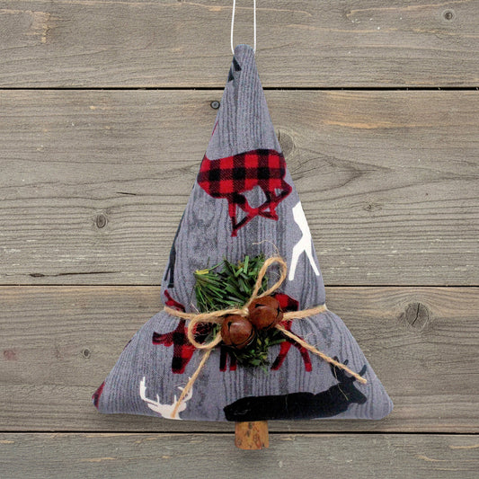 A fabric Christmas tree ornament made from gray corduroy with red and black buffalo plaid forest animals, green pine branches, and two rusty bells tied with twine, hanging against a rustic wood plank background.