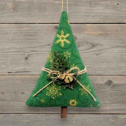 A handmade Christmas tree ornament with gold snowflake patterns, twine bow, small gold bells, and faux greenery, hanging against a rustic gray wooden plank background.
