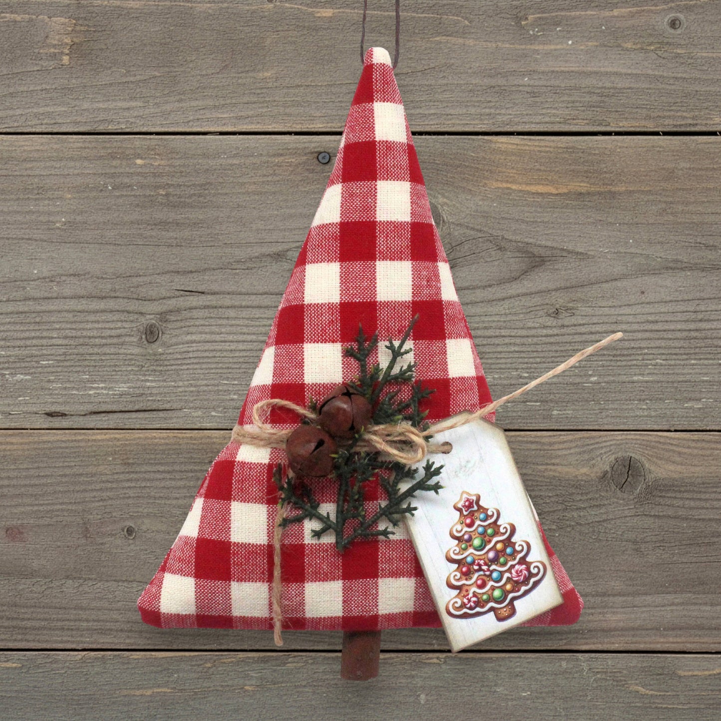 Christmas tree-shaped ornament handmade from red and white homespun fabric with rusty bells and a tag
