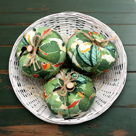 Three green fabric pumpkins with bird patterns on a white woven basket.