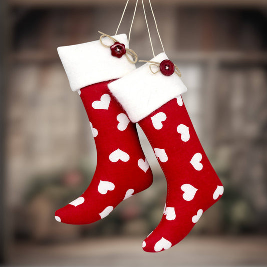Two red Christmas stockings with white hearts and white fleece trim, hanging against a blurred warm-toned background.