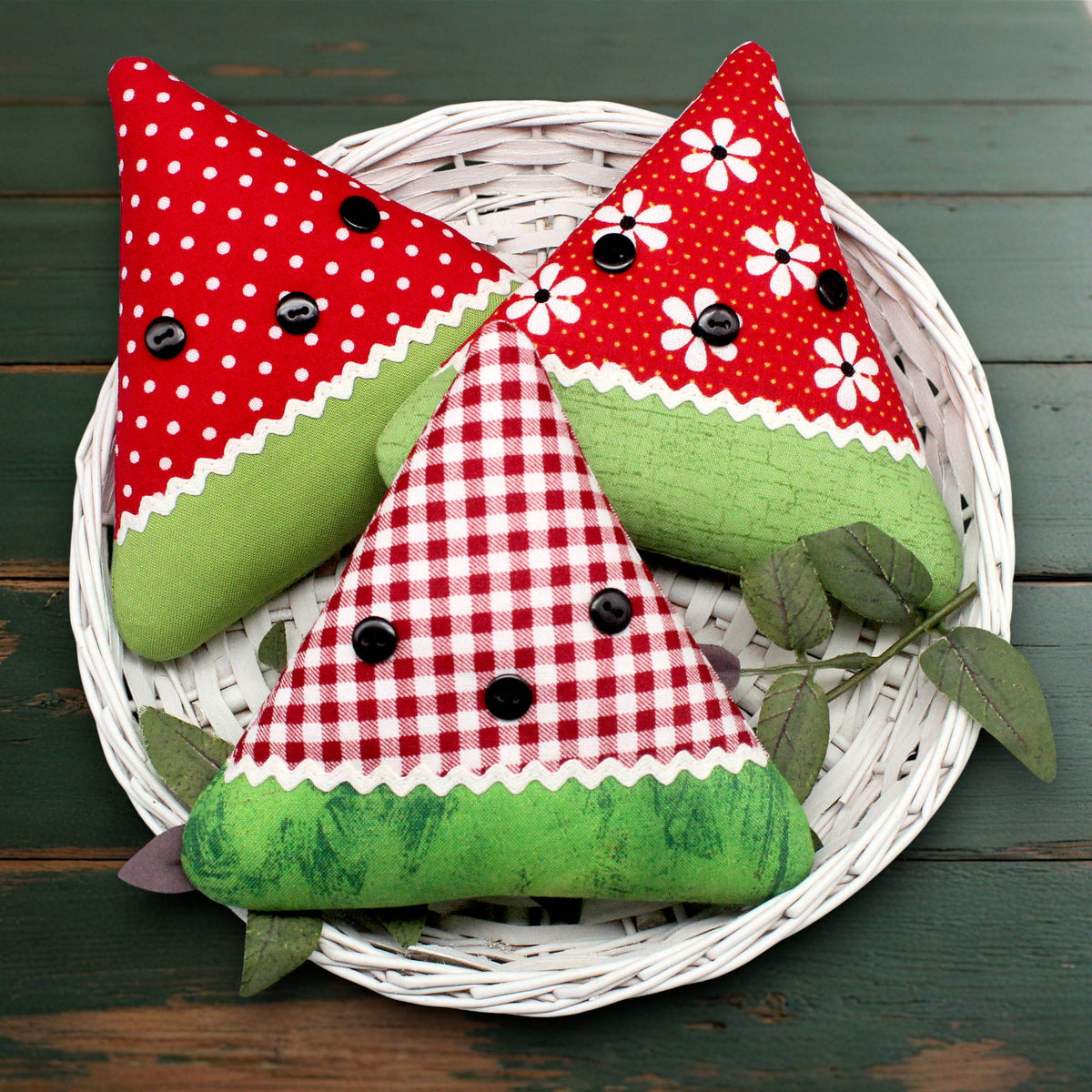 Set of three fabric watermelon slices sewn from coordinating red print fabrics and trimmed with white rick rack and black buttons.