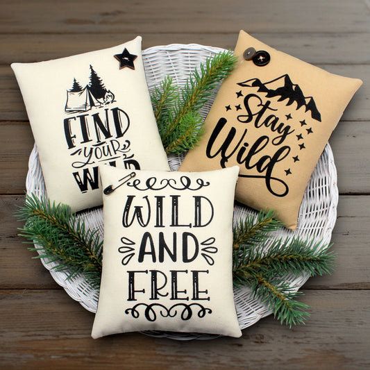 Three pillows with motivational phrases on a wooden surface with greenery.