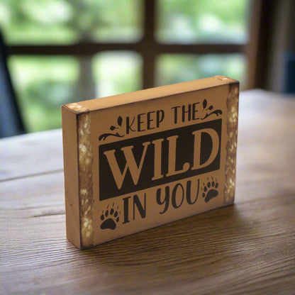 Wooden block with 'Keep the Wild in You' text on a wooden surface