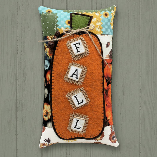 Decorative pillow with 'Fall' text and pumpkin design on a wooden surface